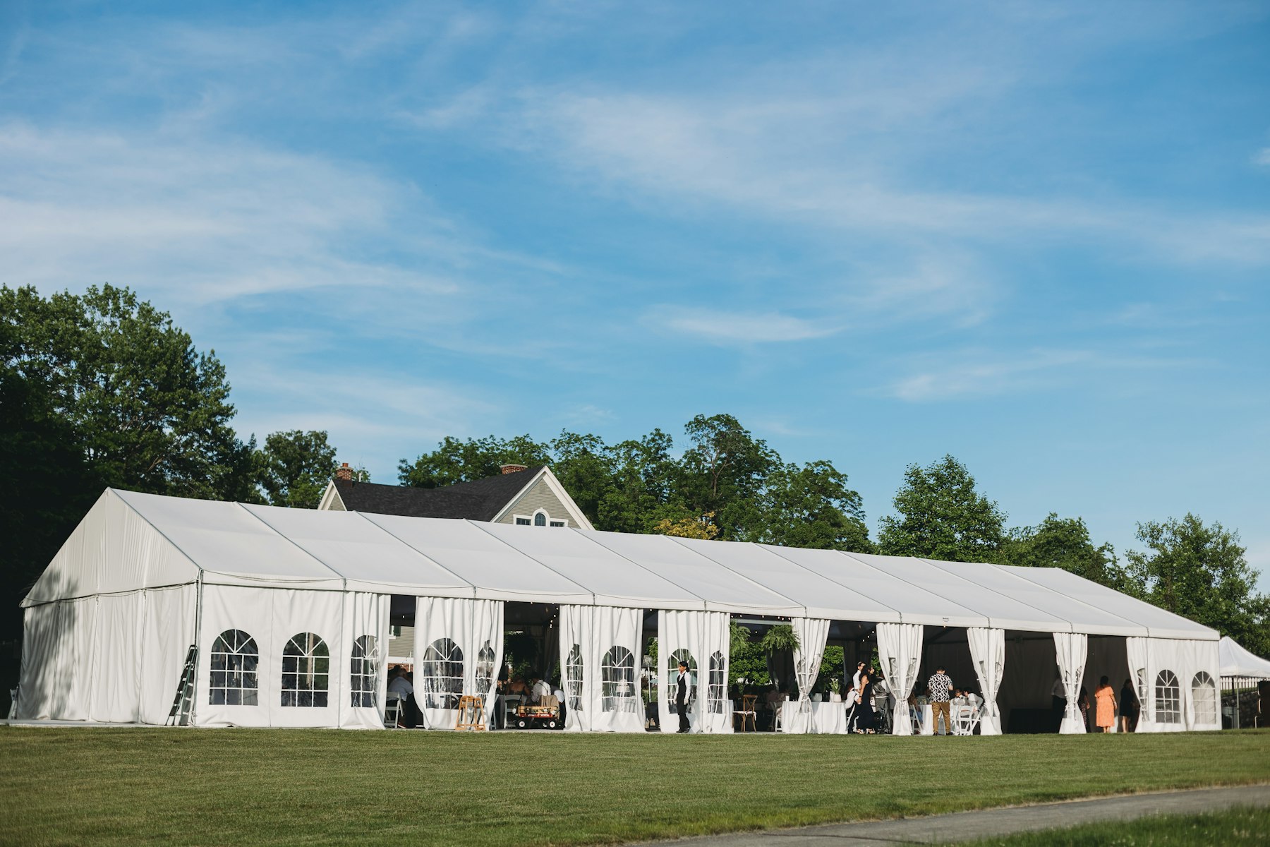 Long white event tent with arched windows on a lawn under blue sky; daytime, not dusk.
