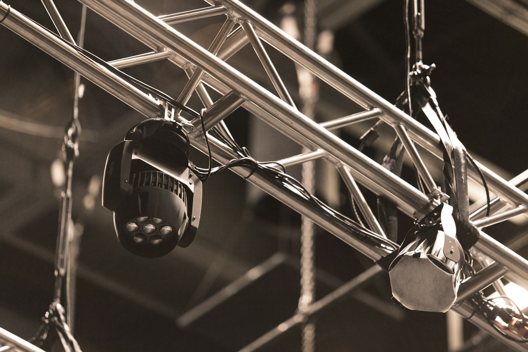 Close view of silver truss with hanging moving-head lights, shown in warm sepia tones.